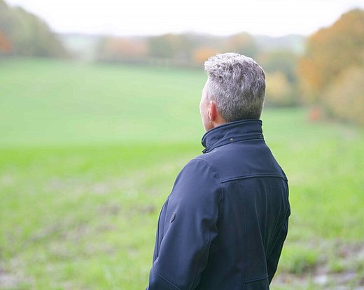 Eine Frau blickt in eine weite, grüne Landschaft. Sie steht im Freien und scheint den ruhigen Moment in der Natur zu genießen